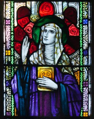 Stained glass window with St Ita clothed in a purple robe and holding a book.