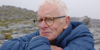 A photograph of Cormac Ó Gráda resting his head on crossed arms with rocky terrain in the background.