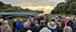 Walking tour group gathered by a foot bridge with a sun set in the background