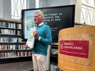 Howard Clarke, standing in Cork City Library holding an atlas