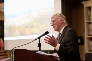 Howard Clarke speaking in front of a screen with an painting of Cork.