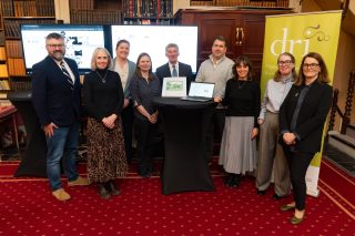 Group of IHTA staff and editors with DRI staff standing by a computer and some screens with Cork information