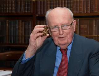 Louis Cullen with his Gold Medal in front of bookshelves